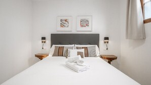 A neatly made bed with white linens and a folded towel, two framed artworks on the wall, and bedside lamps on wooden nightstands. - VINTAGE PALMA PALACE (GRAND DELUXE) by Priority (Palma de Mallorca)