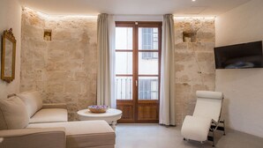 A room with a stone wall, a sofa, a chair, a small table with a bowl, and a TV mounted on the wall. - VINTAGE PALMA PALACE (GRAND DELUXE) by Priority (Palma de Mallorca)