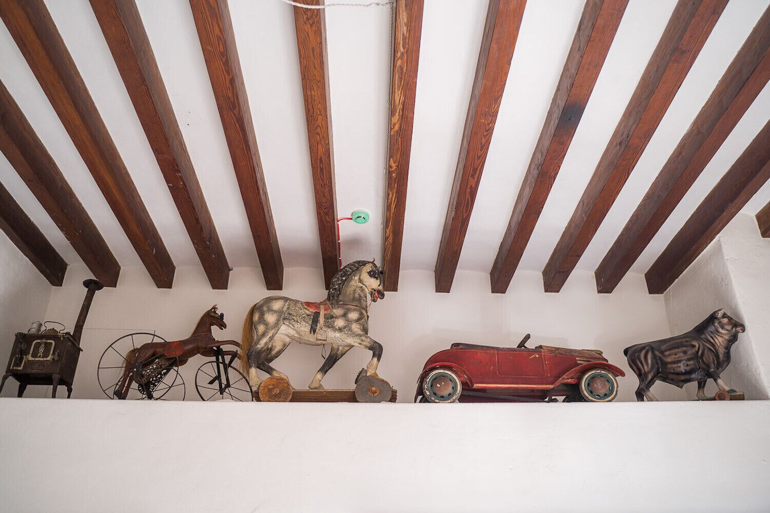 A wooden ceiling with exposed beams and a white wall with a row of vintage toys.