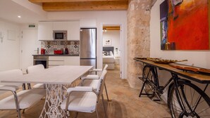 Une cuisine moderne avec des armoires blanches, un réfrigérateur en acier inoxydable et un four à micro-ondes. On y trouve un coin repas avec une table et des chaises blanches. Un vélo est garé à côté de la table.