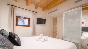Une chambre à coucher avec un lit, un téléviseur fixé au mur et une fenêtre avec des rideaux.