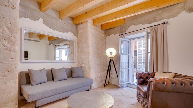 Un salon avec un canapé gris, un canapé en cuir marron, un pouf rond, une lampe sur pied et un grand miroir accroché au mur.