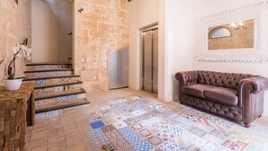 Une pièce spacieuse dotée d’un sol carrelé, d’un canapé en cuir marron, d’un escalier aux carreaux décoratifs et d’un miroir fixé au mur.