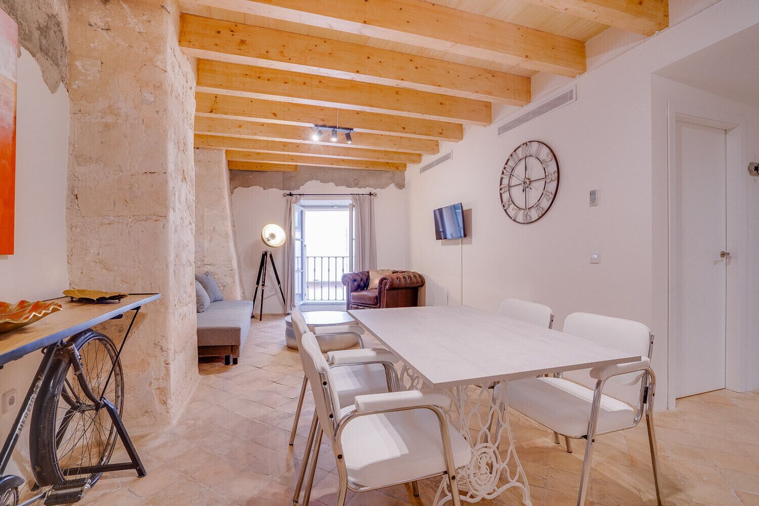 A spacious room with a large dining table, white chairs, a sofa, and a bike.