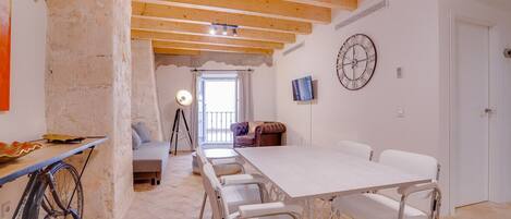 A spacious room with a large dining table, white chairs, a sofa, and a bike.