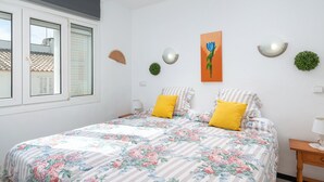 Une chambre à coucher avec une couvre-lit à motifs floraux, deux oreillers, une lampe fixée au mur et un tableau.
