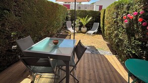 Une terrasse dotée d’une table à plateau en verre, de deux chaises, d’un grand parasol et d’une plateforme en bois.