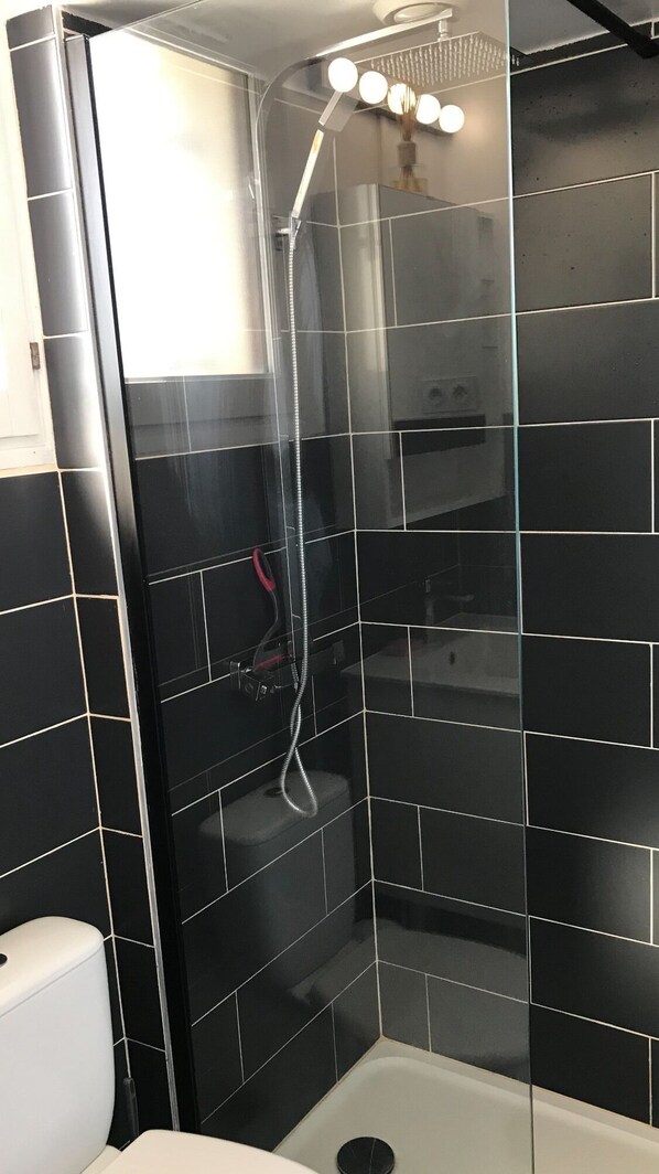 A bathroom with black tiled walls, a glass shower enclosure, and a white toilet. - Apartment 4 persons-RDC-Jardinet 20m2- Private parking - 200m beach (Vaux-sur-Mer)