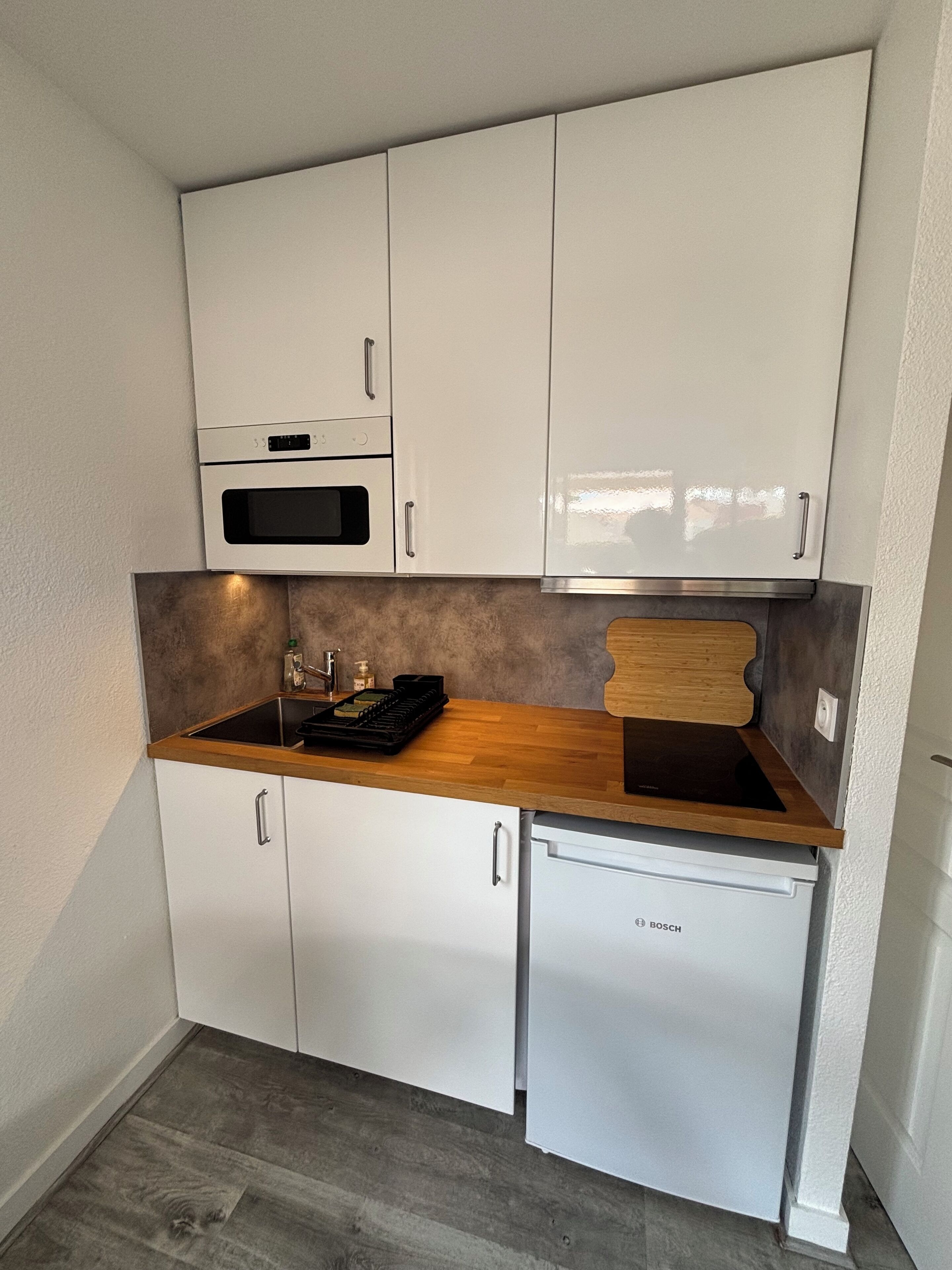 A compact kitchen with white cabinets, a Bosch dishwasher, and a wooden countertop.