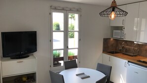 Une cuisine compacte avec des meubles blancs, un four à micro-ondes, un lave-vaisselle Bosch et un coin repas comprenant une table et des chaises.