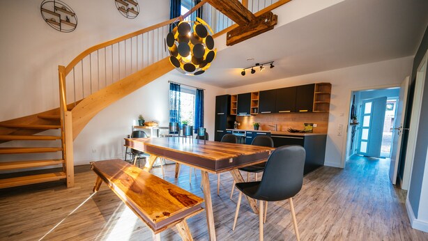 A spacious kitchen with modern appliances, a dining area with a wooden table and bench, and a staircase with wooden railings.