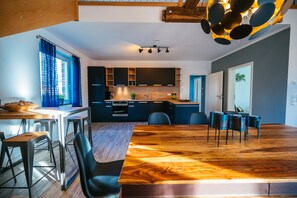 Une cuisine moderne avec des meubles de couleur sombre, une table à manger en bois et une grande fenêtre ornée de rideaux bleus.