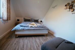 Une chambre avec un plancher en bois, un lit recouvert d’une courtepointe bleue et blanche, deux tables de chevet avec des lampes et une décoration murale représentant une tête de cerf.