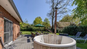 A backyard with a wooden hot tub, outdoor furniture, and a patio area.