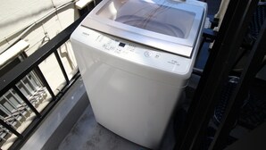 A front-loading washing machine on a balcony with a metal railing. - Xiaoningge (Osaka)