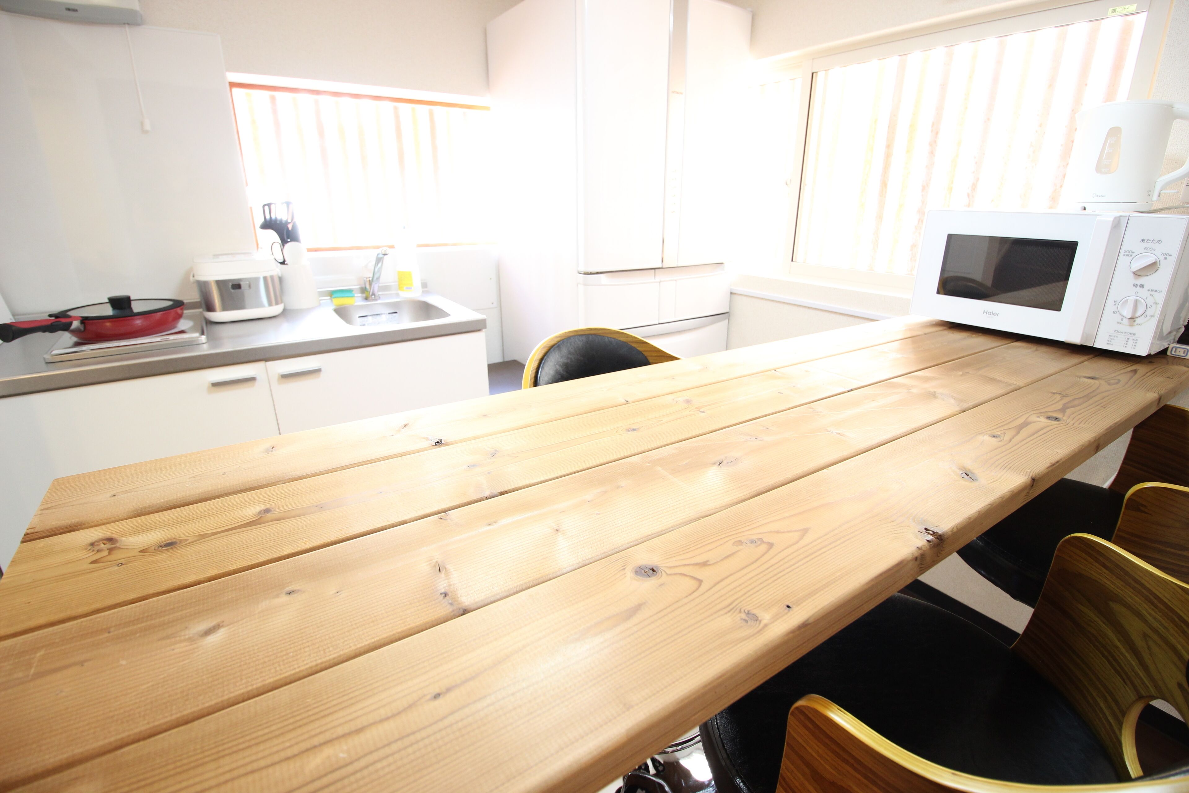 A kitchen with a wooden table, white cabinets, a microwave, and a red pan.