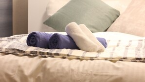 A bed with rolled towels and pillows, a checkered blanket, and a window with vertical blinds. - Xiaoningge (Osaka)