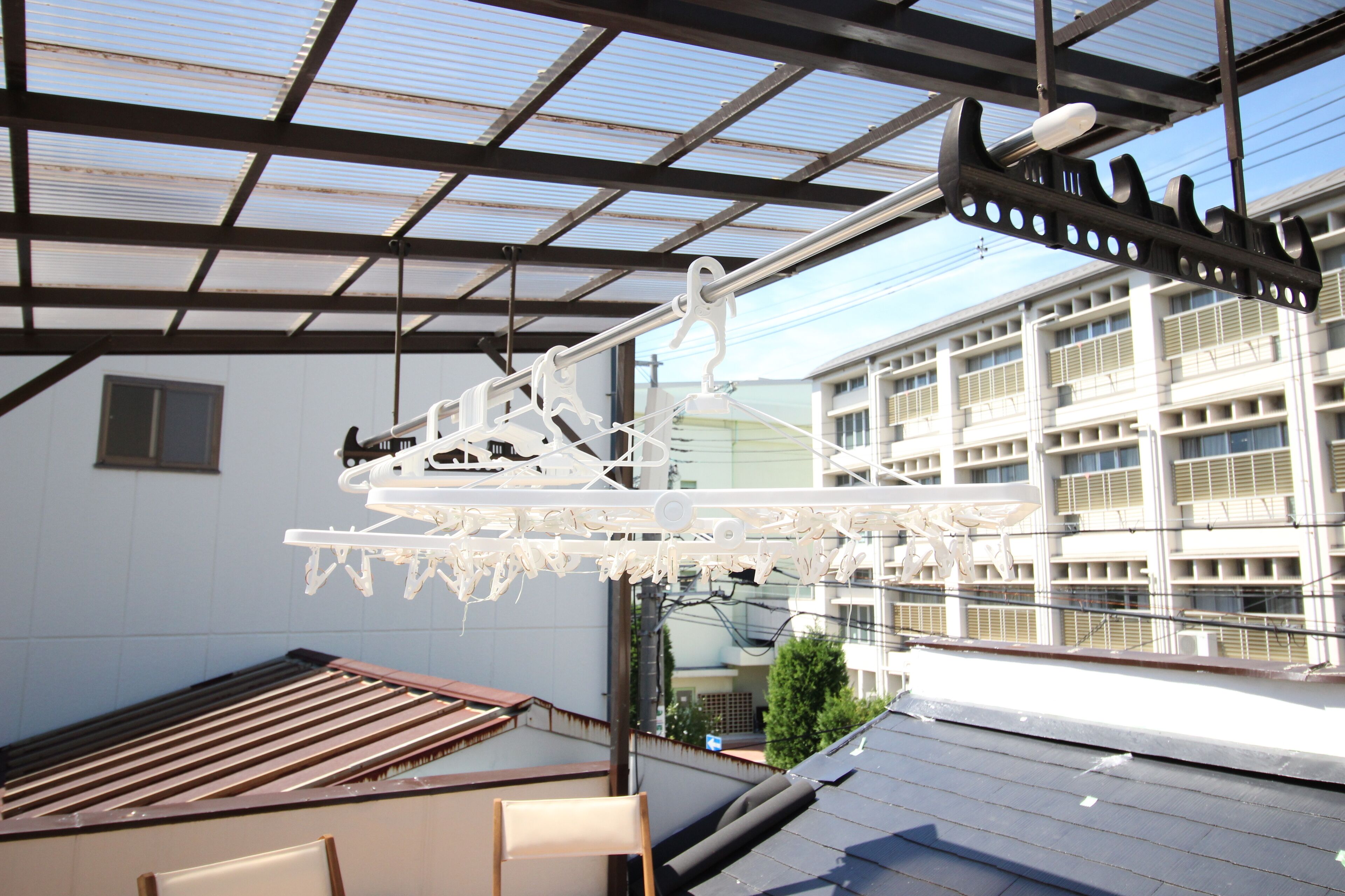A rooftop terrace with a metal roof structure, a hanging light fixture, and a view of a building with multiple windows.
