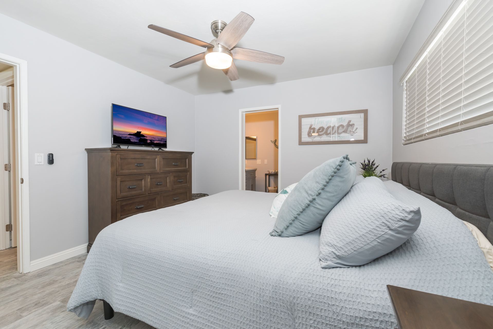 A bedroom with a bed, a ceiling fan, a dresser, a television, and a framed quote on the wall.