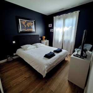 Een slaapkamer met een bed, een bureau met een computer, een wereldkaart aan de muur, en een raam met gordijnen.