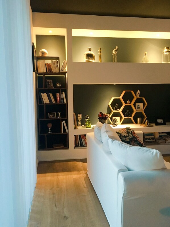 A modern living room with a white sofa, a bookshelf, and a decorative hexagonal shelf with various items.