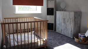 A baby room with a wooden crib, a cabinet, and a window with blinds. - Apartment 1 - Apartment Rosenstadt (Forst (Lausitz))