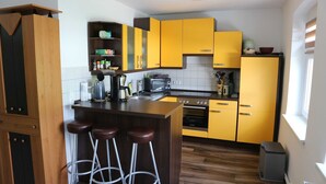 A kitchen with yellow cabinets, a wooden island with stools, a microwave, and a stove. - Apartment 2 - Apartment Rosenstadt (Forst (Lausitz))