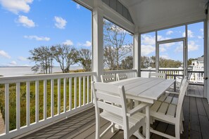 A covered outdoor deck with a white table and chairs, overlooking a body of water and trees. - SOUNDFRONT with Private Pier! Private Pool, Dogs ok! (Corolla)