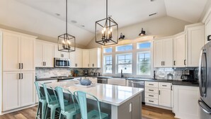 A modern kitchen with white cabinets, a large island with bar stools, stainless steel appliances, and pendant lighting.