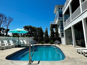 A swimming pool with a white deck, a turquoise umbrella, and white lounge chairs. - SOUNDFRONT with Private Pier! Private Pool, Dogs ok! (Corolla)