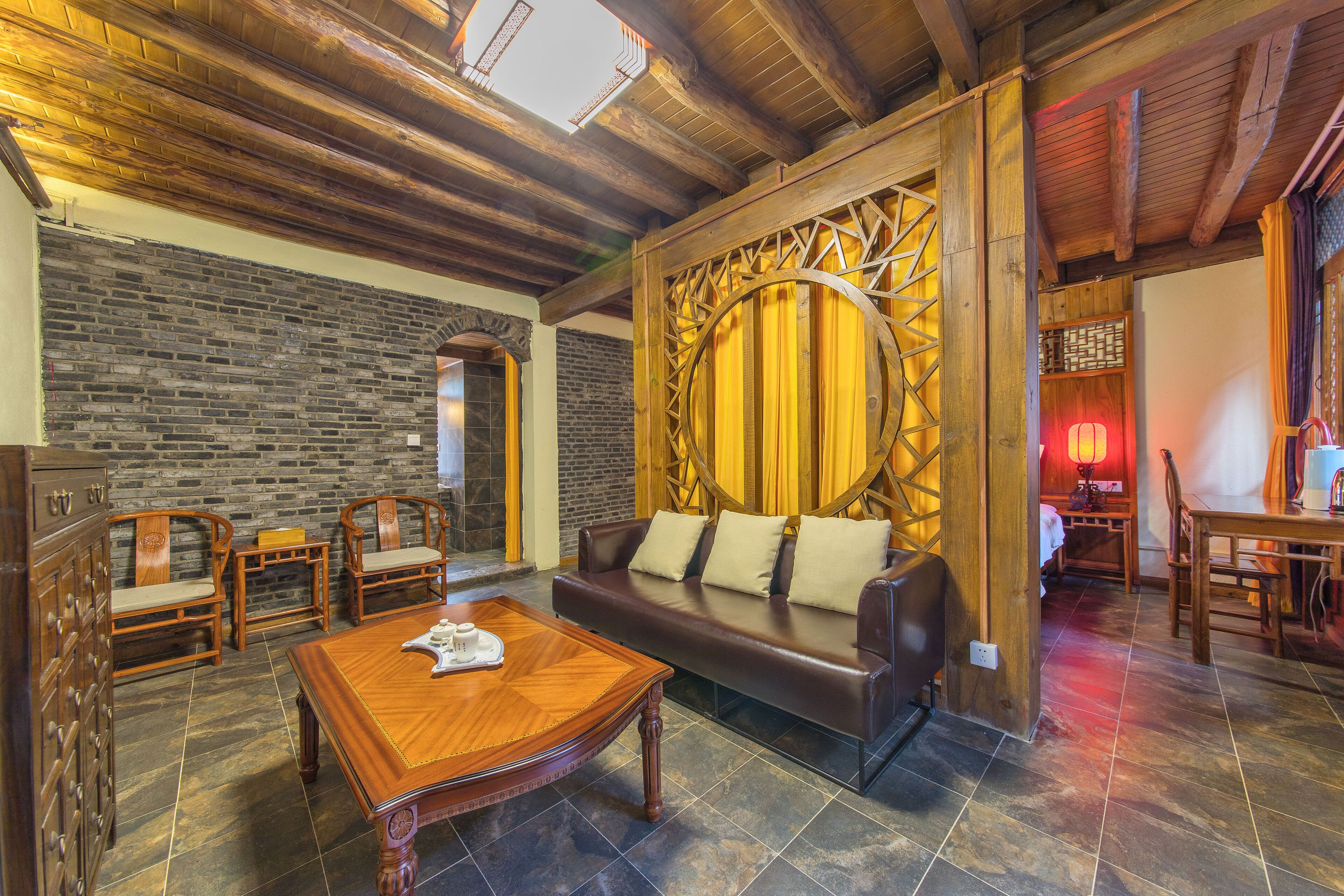 A cozy room with a wooden ceiling, a stone wall, a leather sofa, wooden chairs, and a wooden coffee table.