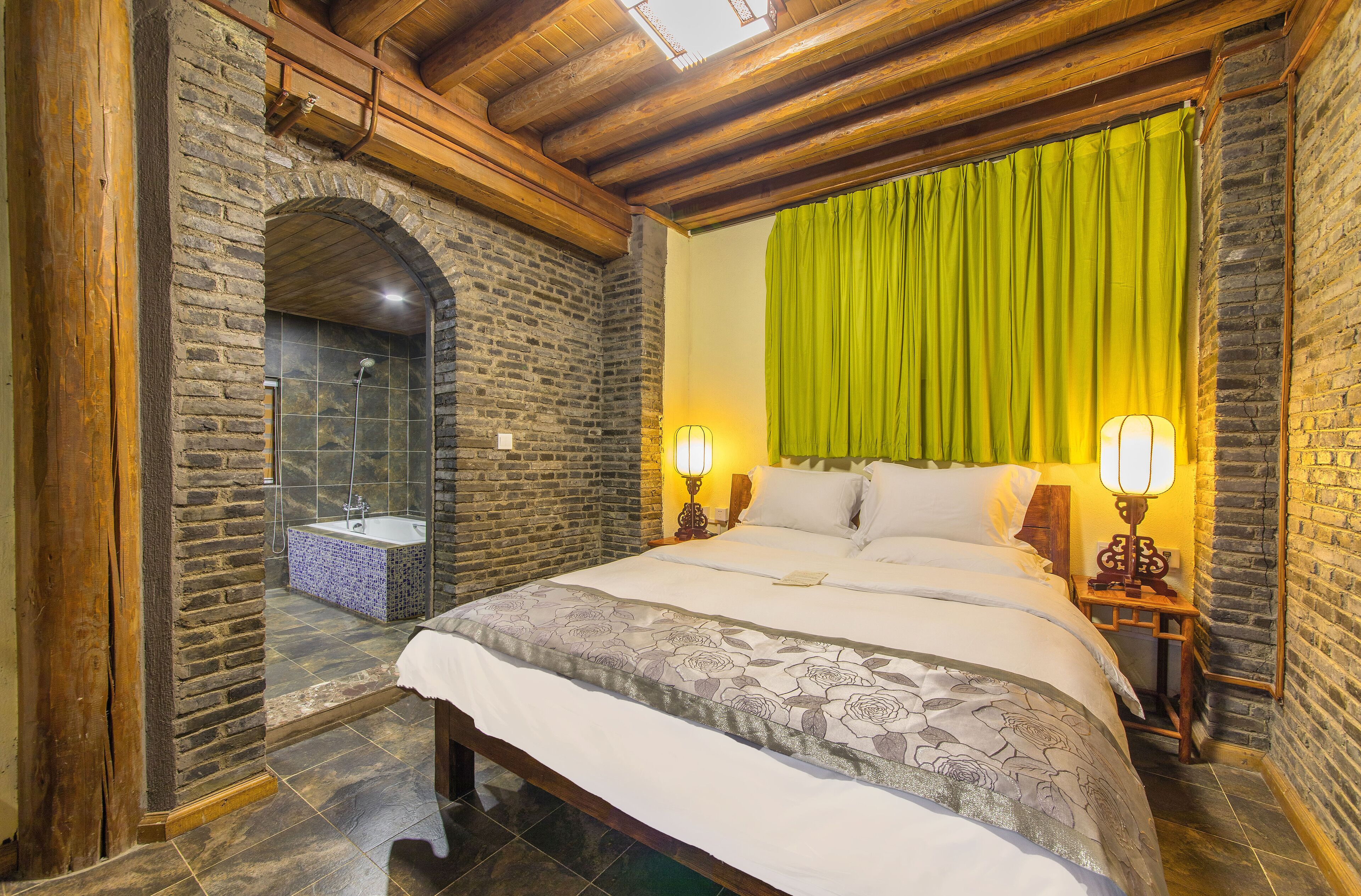 A bedroom with a large bed, a wooden ceiling, a stone wall, and a green curtain.