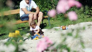 A person sitting on a bench in a park with sand and toys.