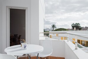 A balcony with a white table and chairs, a door, and a view of buildings and palm trees.