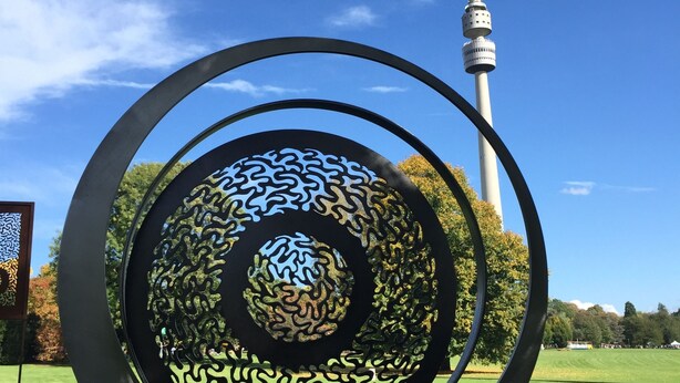 A metal sculpture with concentric circles and a tower in the background.