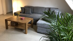 A cozy living room with a grey sofa, a wooden coffee table, and a large green plant.