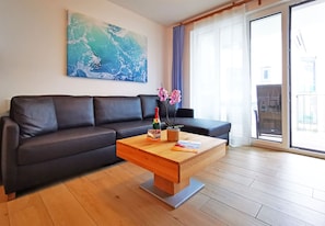 A modern living room with a dark leather sofa, a wooden coffee table, and a large abstract painting on the wall. - Baabe Villen Ensemble FeWo 30 Strandzeit Ref. 212638 (Baabe)