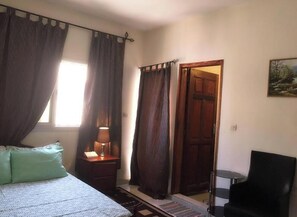 Une chambre à coucher avec un lit, une table de chevet, une lampe, une chaise et une porte.