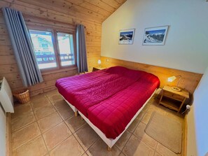 Ein Zimmer mit Holzwänden, einem Bett, zwei Nachttischen, einem Fenster mit Vorhängen und zwei gerahmten Bildern an der Wand.