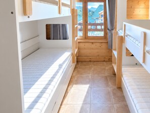 A bunk bed room with a window view of a building and a wooden staircase.