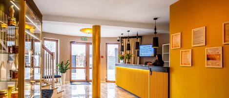 A hotel lobby with a reception desk, a glass display case, a staircase, and a large window.