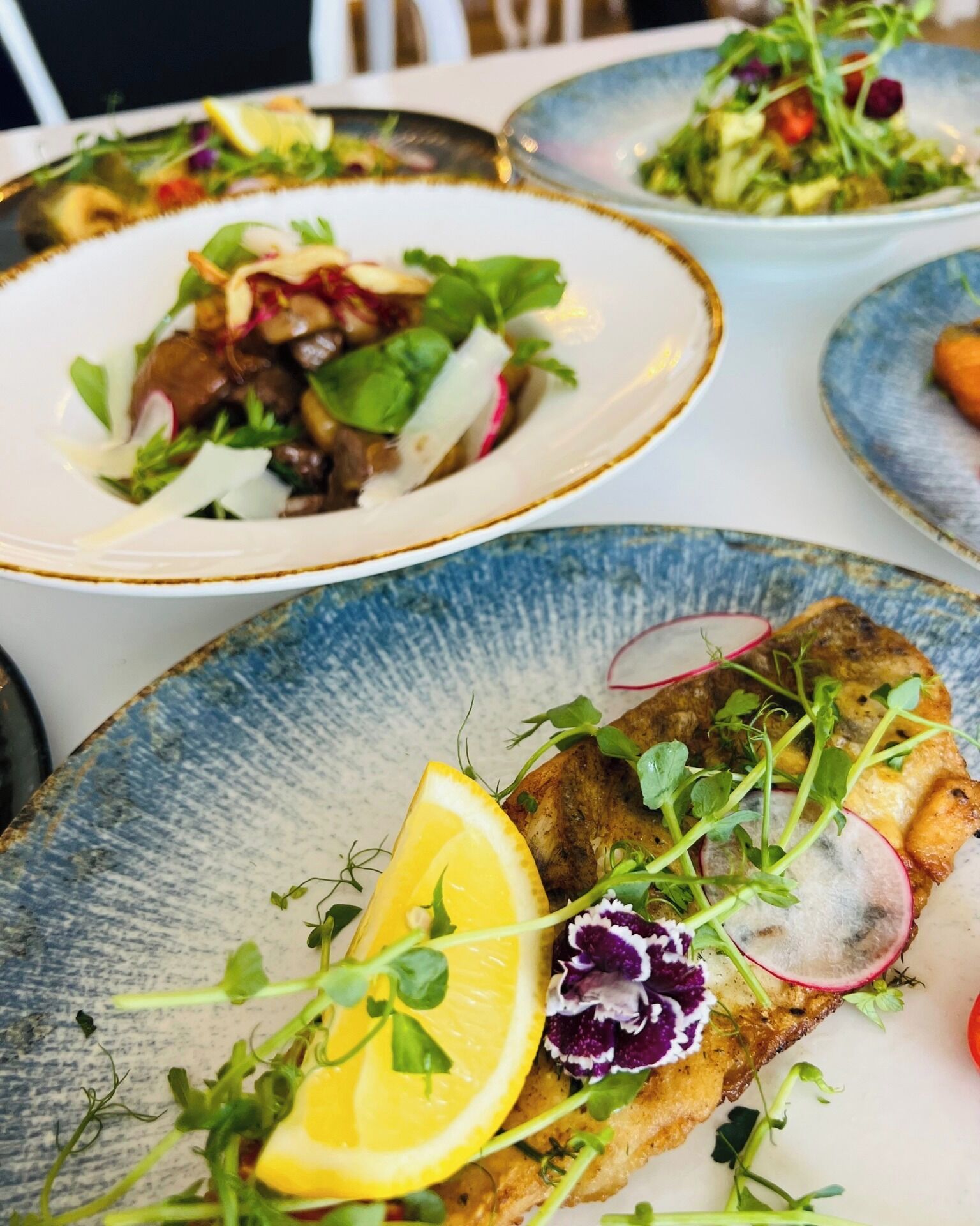 Una mesa de comedor con platos de comida, incluyendo un plato de pescado decorado con limón y hierbas.