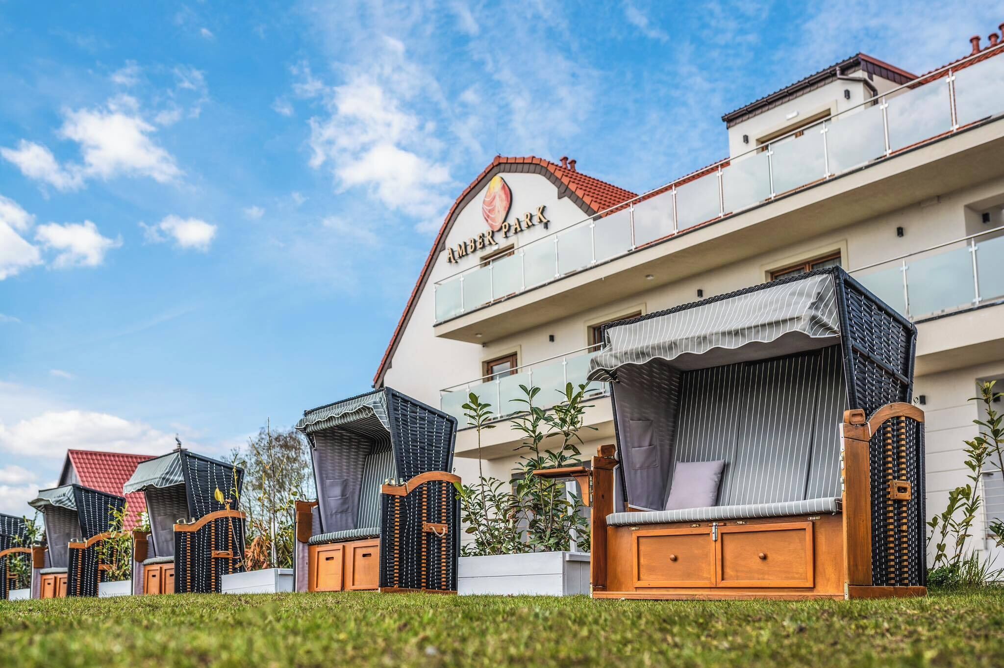 A hotel with a sign reading "Amber Park," featuring outdoor seating areas with wooden furniture and a red-tiled roof.
