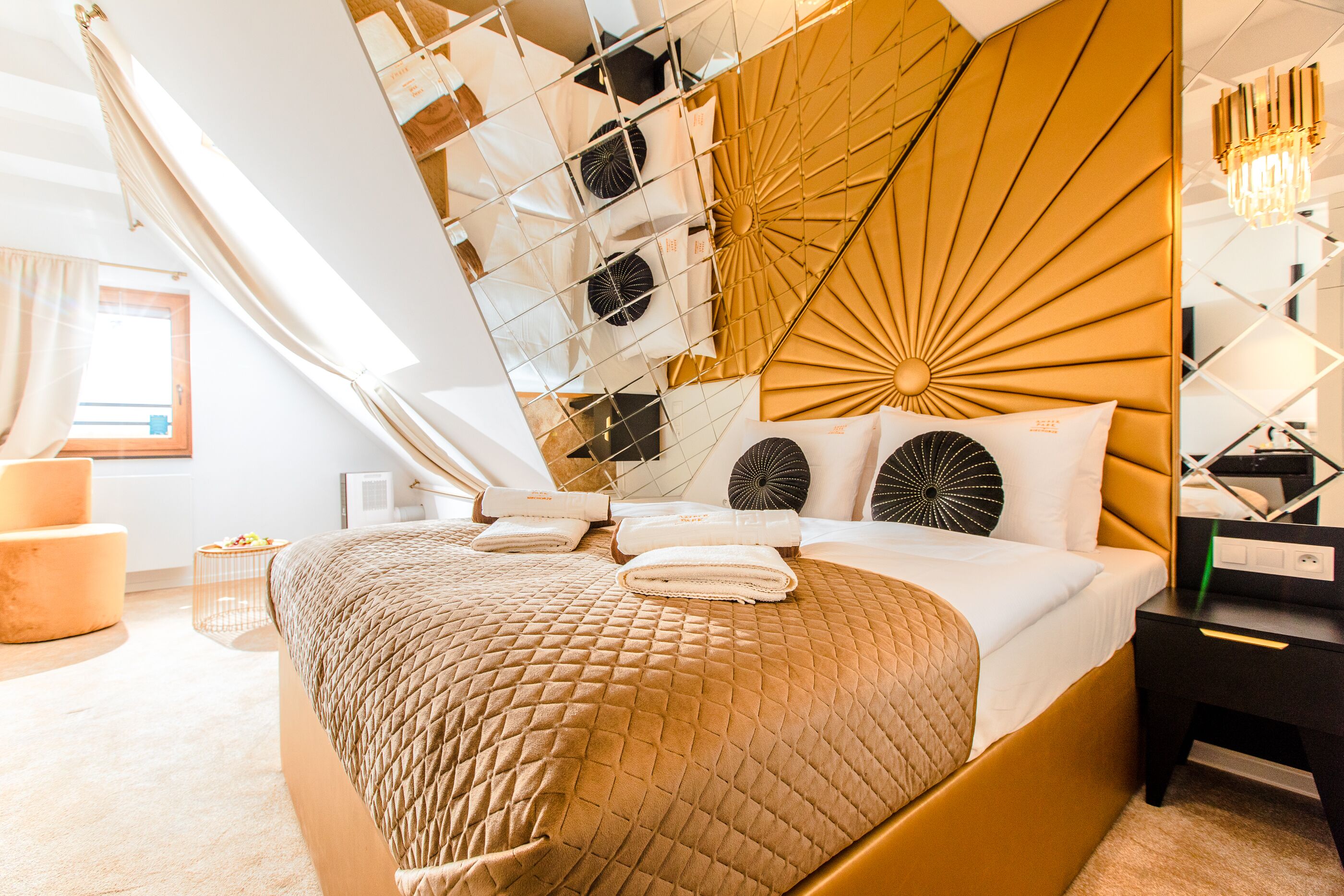 A modern hotel room with a large bed, a headboard with a sunburst design, and a bedside table with a lamp.
