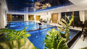 Zona de piscina de hotel con dos piscinas, sillas de descanso y plantas en macetas.