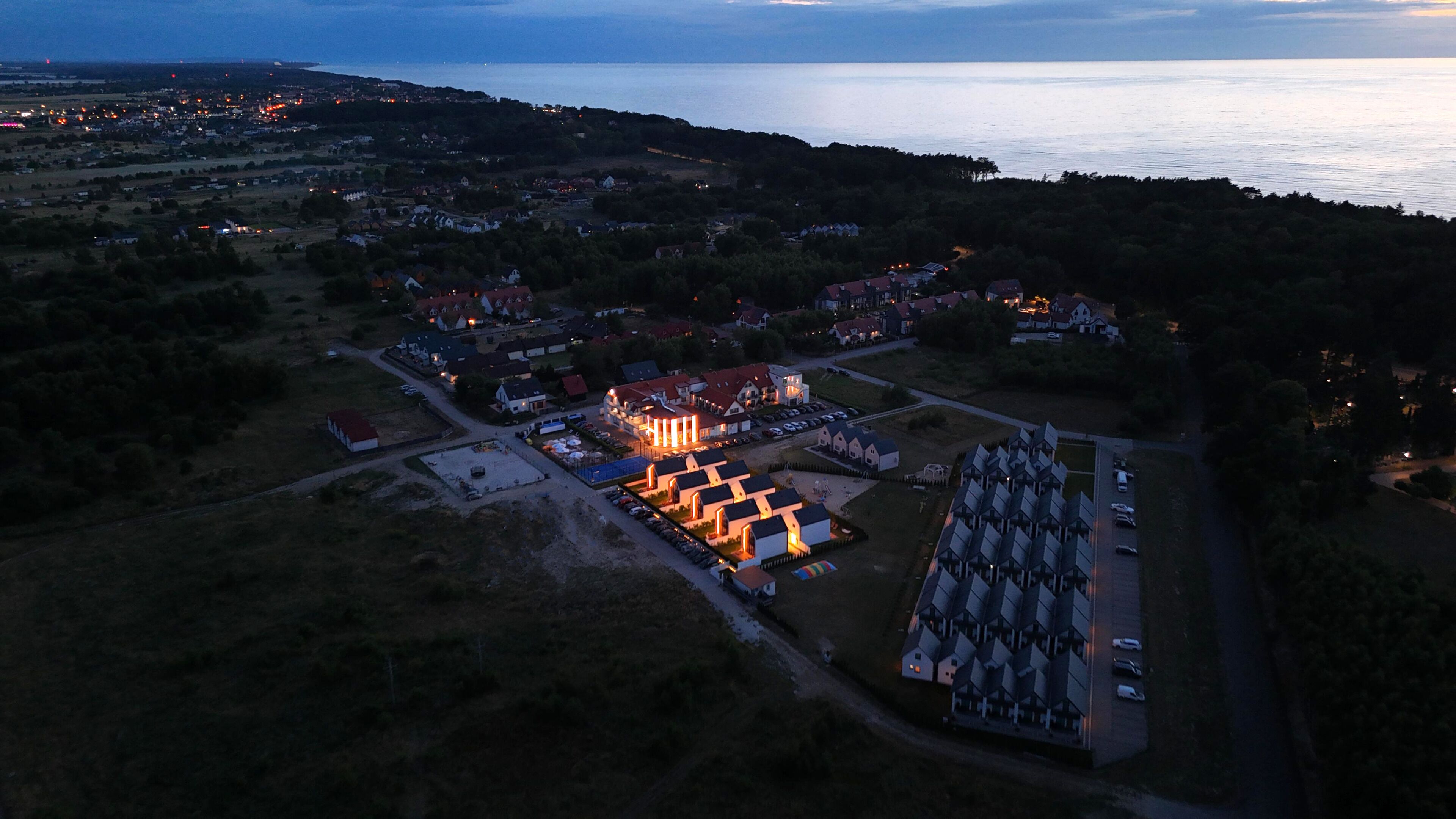 An aerial view of a coastal town at dusk with illuminated buildings and a large church.