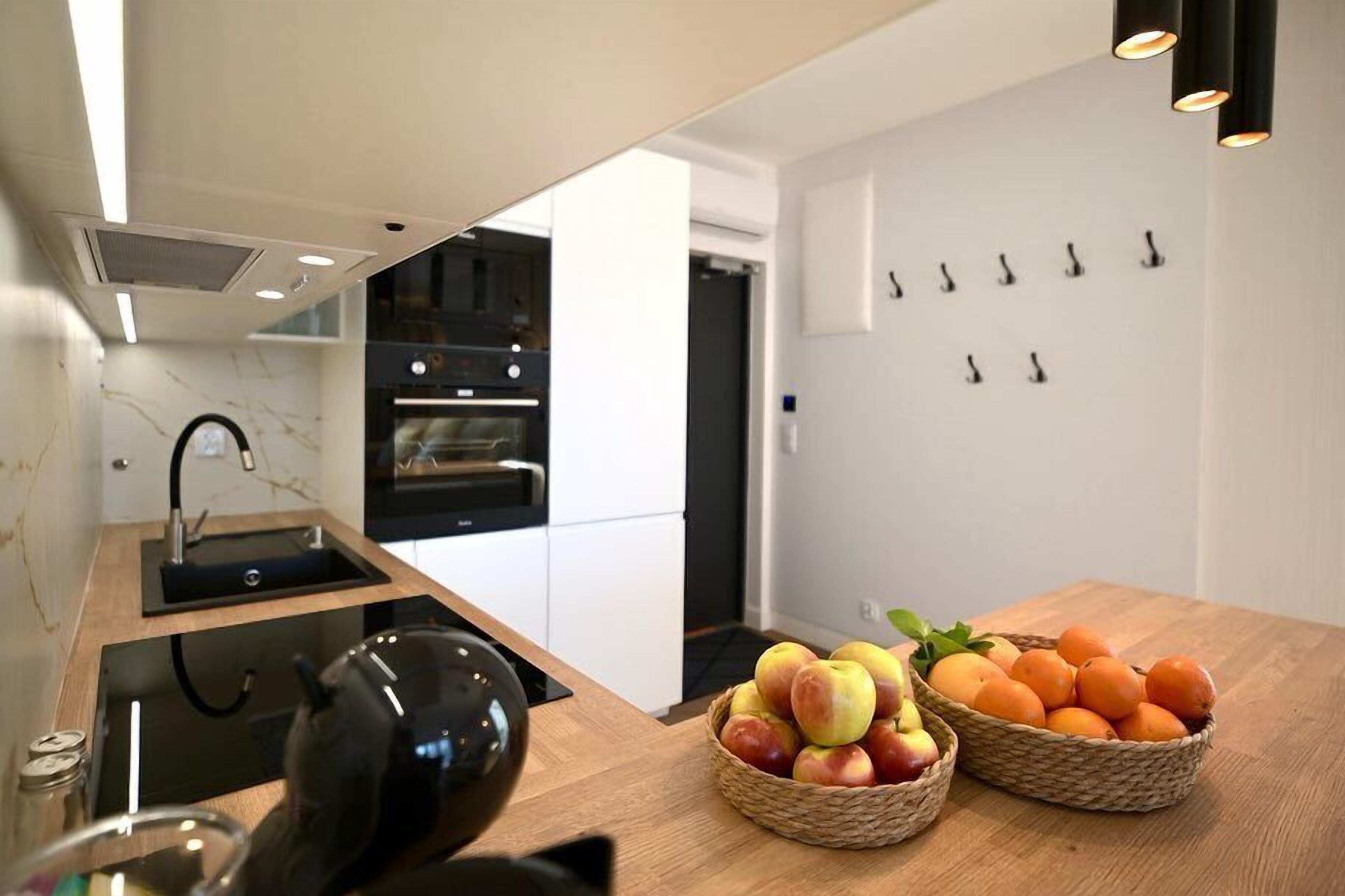 A modern kitchen with a wooden countertop, a black kettle, and baskets of fruit.