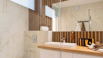 A modern bathroom with a marble floor, a wooden vanity, a white sink, a toilet, and a large mirror.