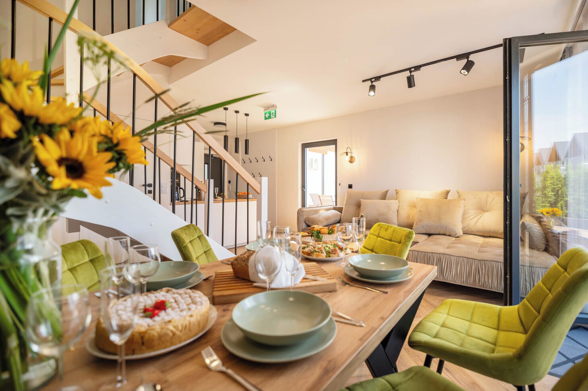 Ein Essbereich mit Holztisch, gedecktem Tisch für eine Mahlzeit, einer Couch mit Kissen und einer Treppe im Hintergrund.