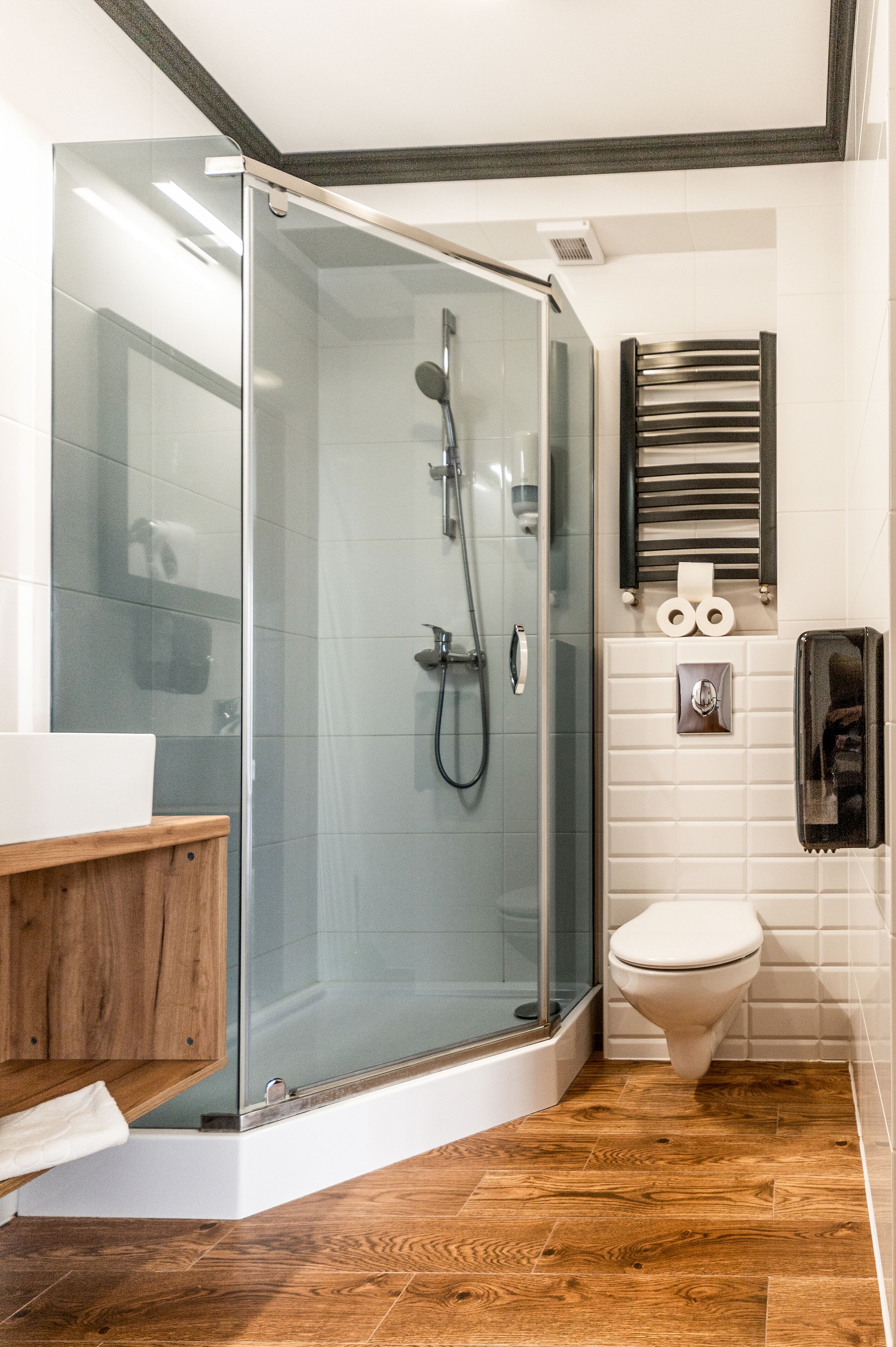 A modern bathroom with a glass-enclosed shower, a wooden vanity, a toilet, and a towel rack.